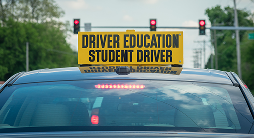 Yellow student driver sign on top of car at stoplight